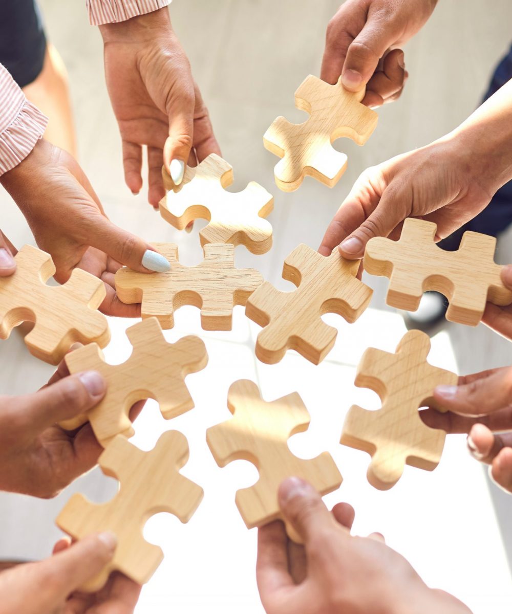 Close up of company workers finding solution in corporate work meeting. Cropped office employees learning to collaborate and playing with pieces of jigsaw puzzle during team building activity